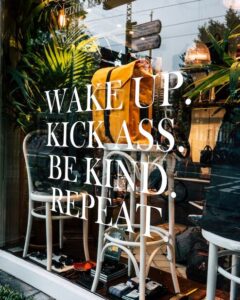 Window with quote saying wake up, kick ass, be kind, repeat as a sign of how to. grow your business