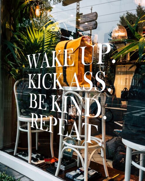 Window with quote saying wake up, kick ass, be kind, repeat as a sign of how to. grow your business